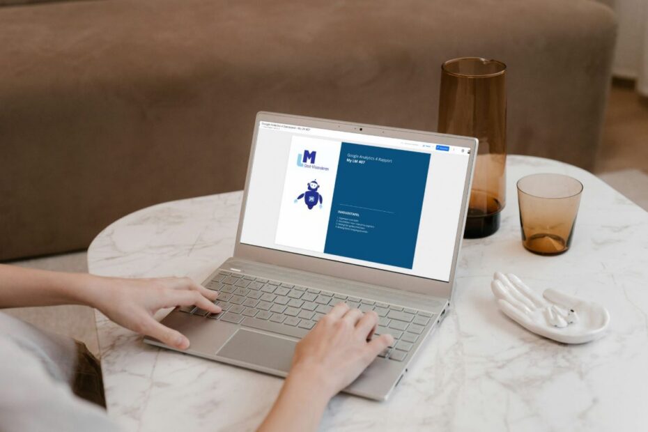 Laptop op een marmeren tafel toont de titelpagina van een Google Analytics 4 rapport in Looker Studio, met het logo van LM Oost-Vlaanderen en een inhoudstafel.